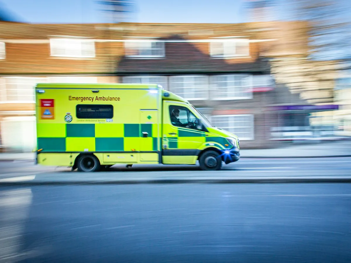 A UK emergency ambulance in green and yellow chequers driving down a street