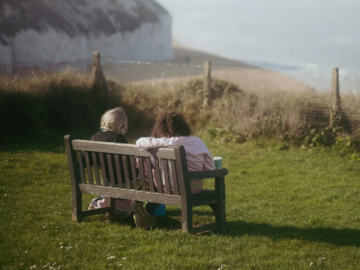 Two people sitting on a bench looking out at white chalk cliffs and the sea