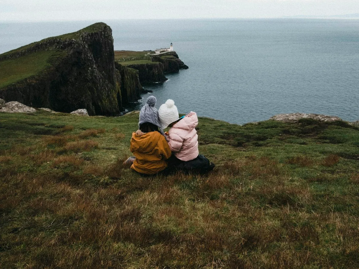 Two people sitting together on a grassy clifftop above the sea