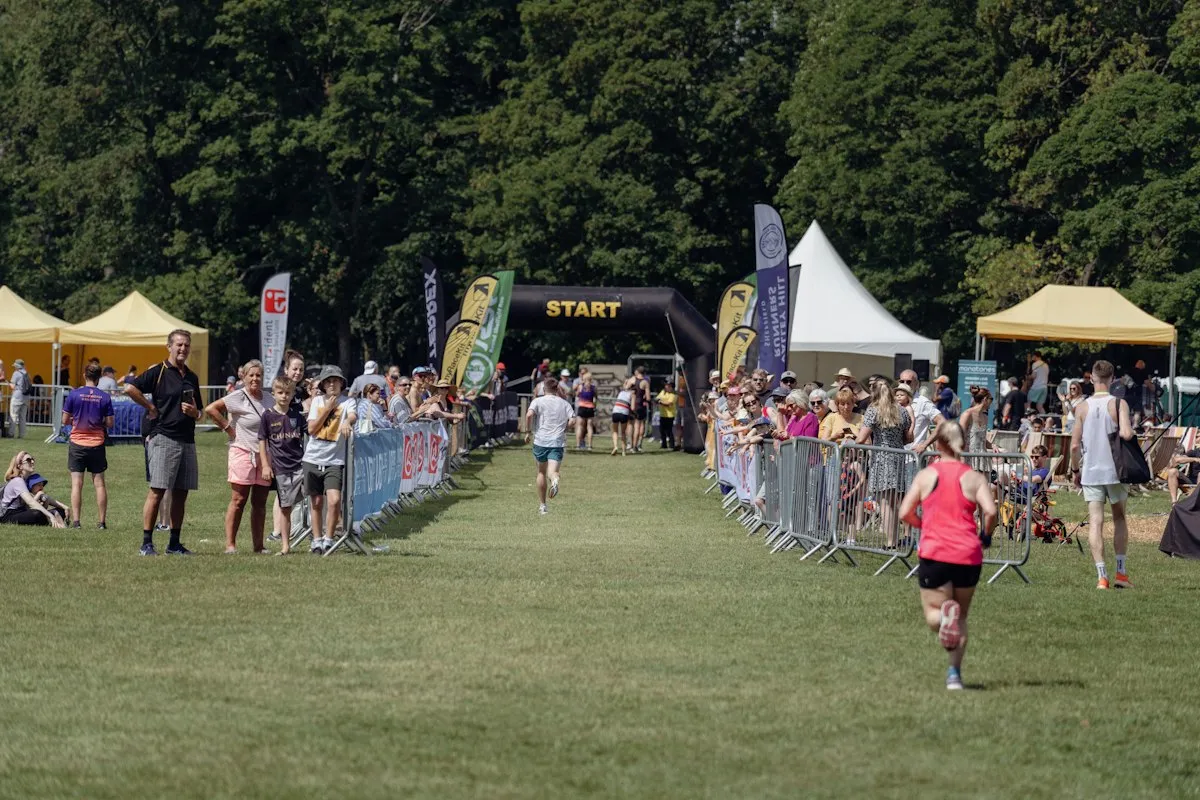 Runners heading for the start arch of a fun run in a leafy British park, cheered on by crowds