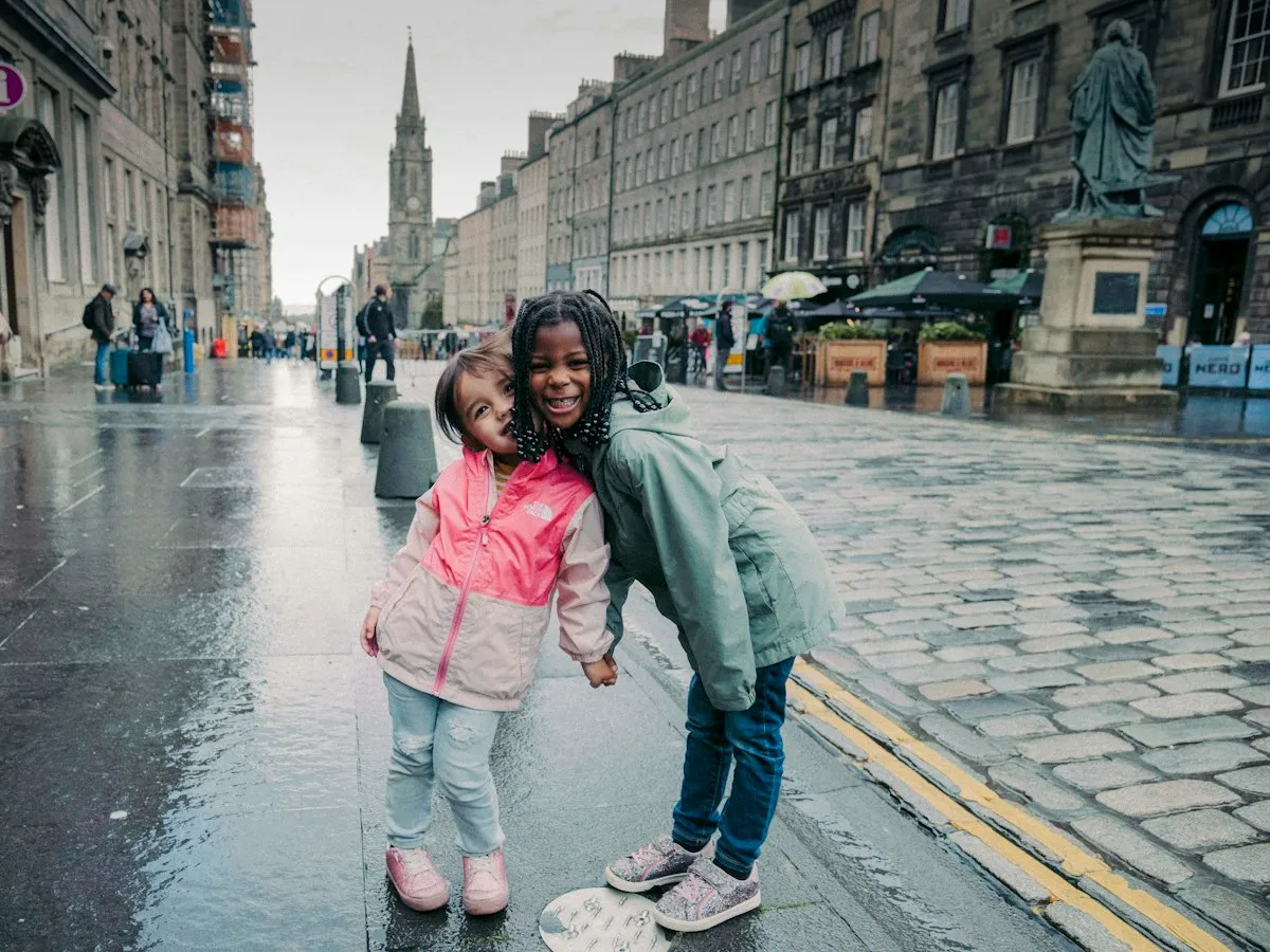 Two children in raincoats laughing on a wet cobbled street