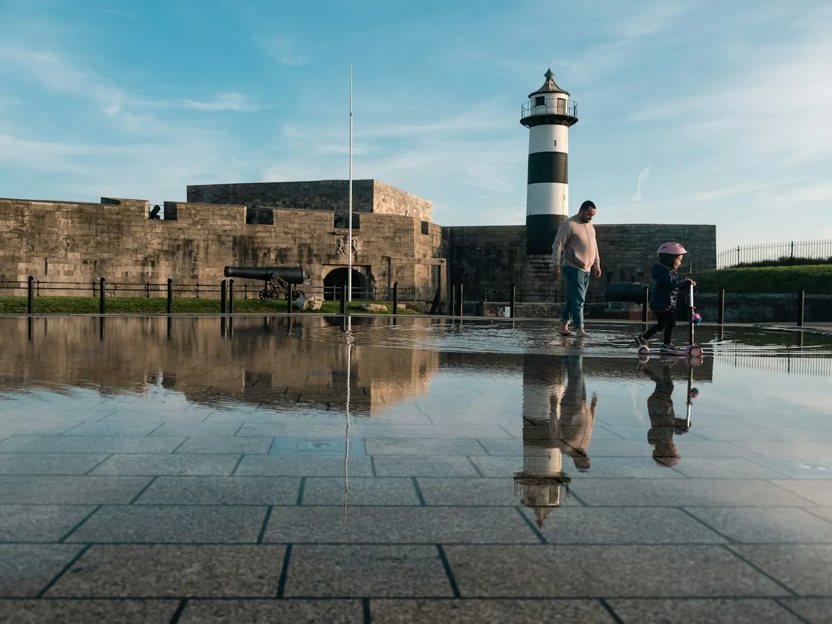 A father and his young daughter on a scooter by Southsea Castle's lighthouse in Portsmouth