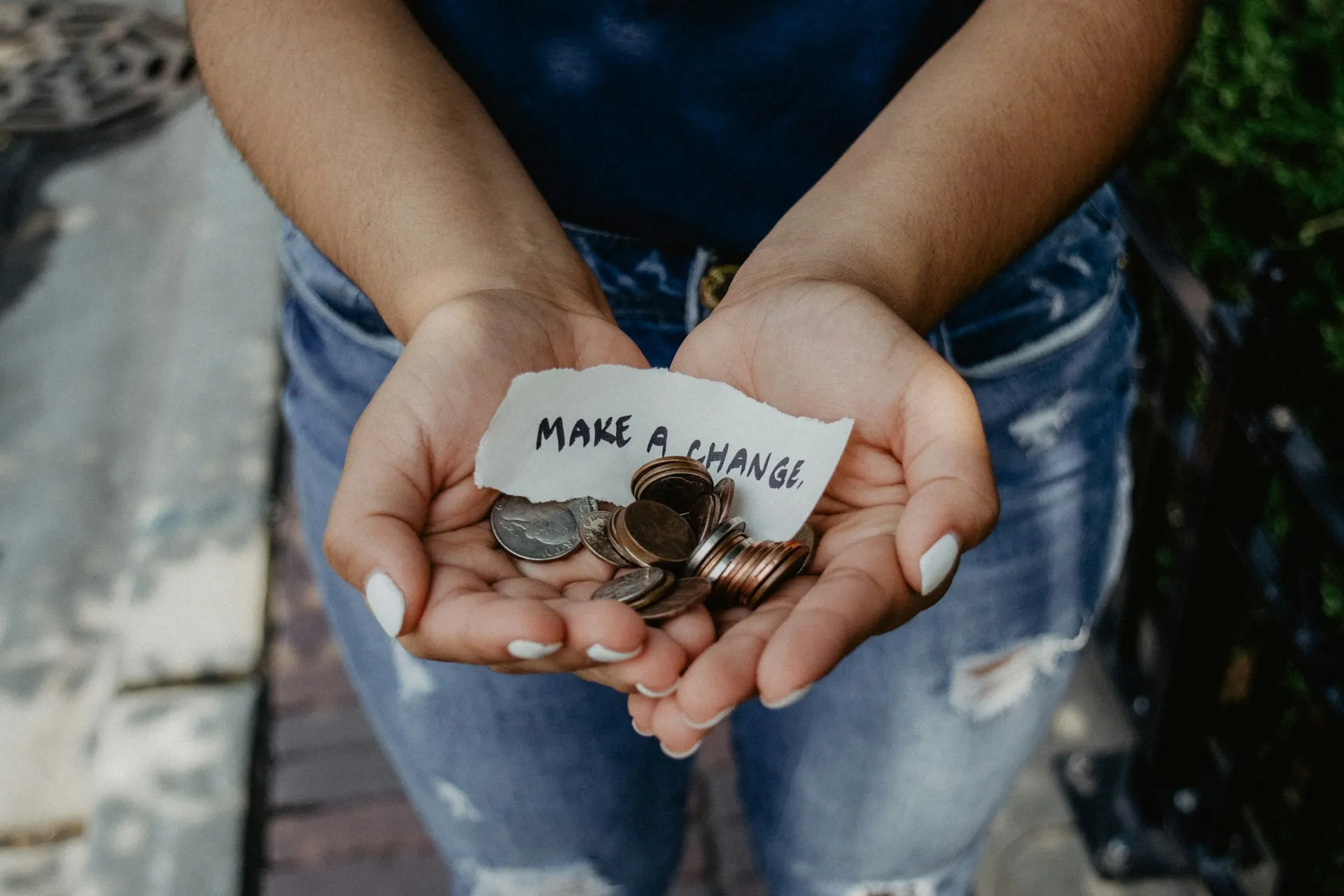 A person's cupped hands holding coins and a handwritten note reading "make a change".